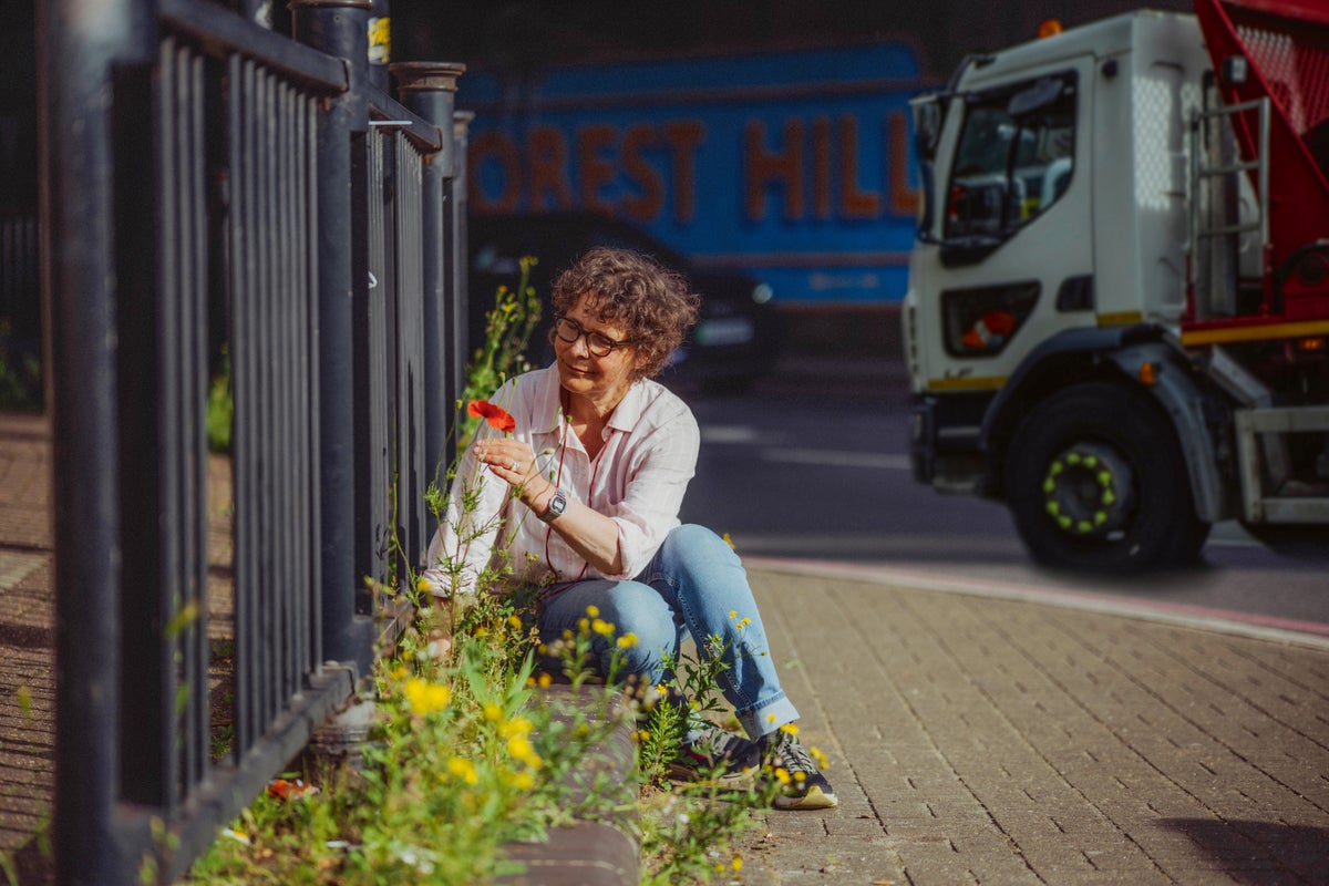 Amanda Tuke kneeling on the sidewalk and holding a red flower