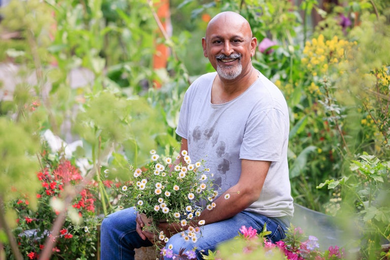 A man sitting in a garden holding a pot of flowers