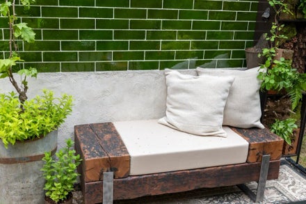 A bench with pillows and plants in front of a wall