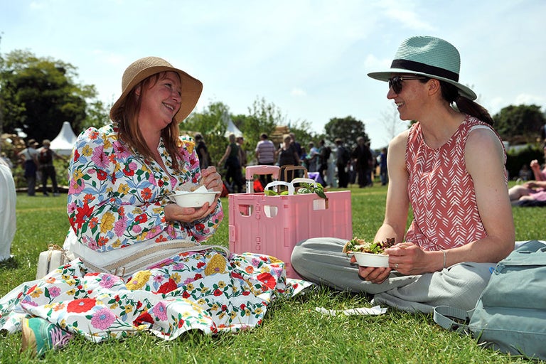 A couple of women sitting on grass eating food