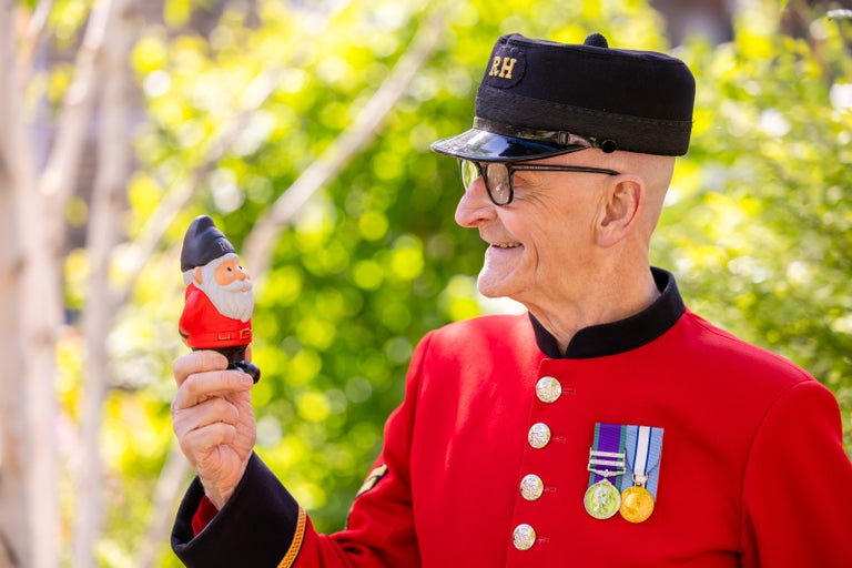 A Chelsea pensioner in a red uniform holding a gnome